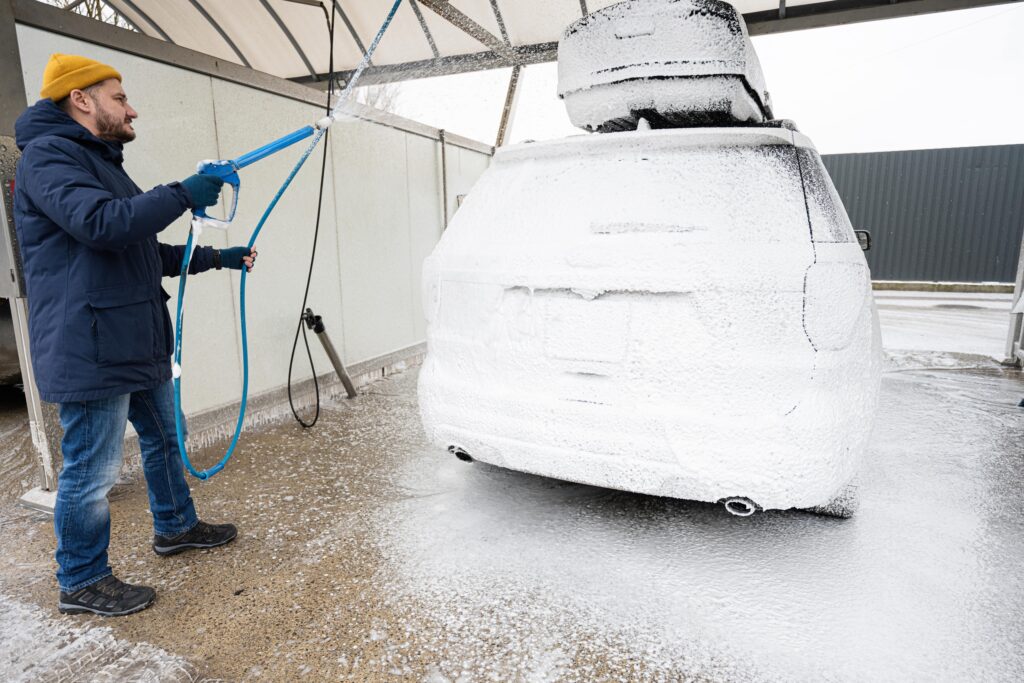 Man washing an SUV with a roof rack at a car wash