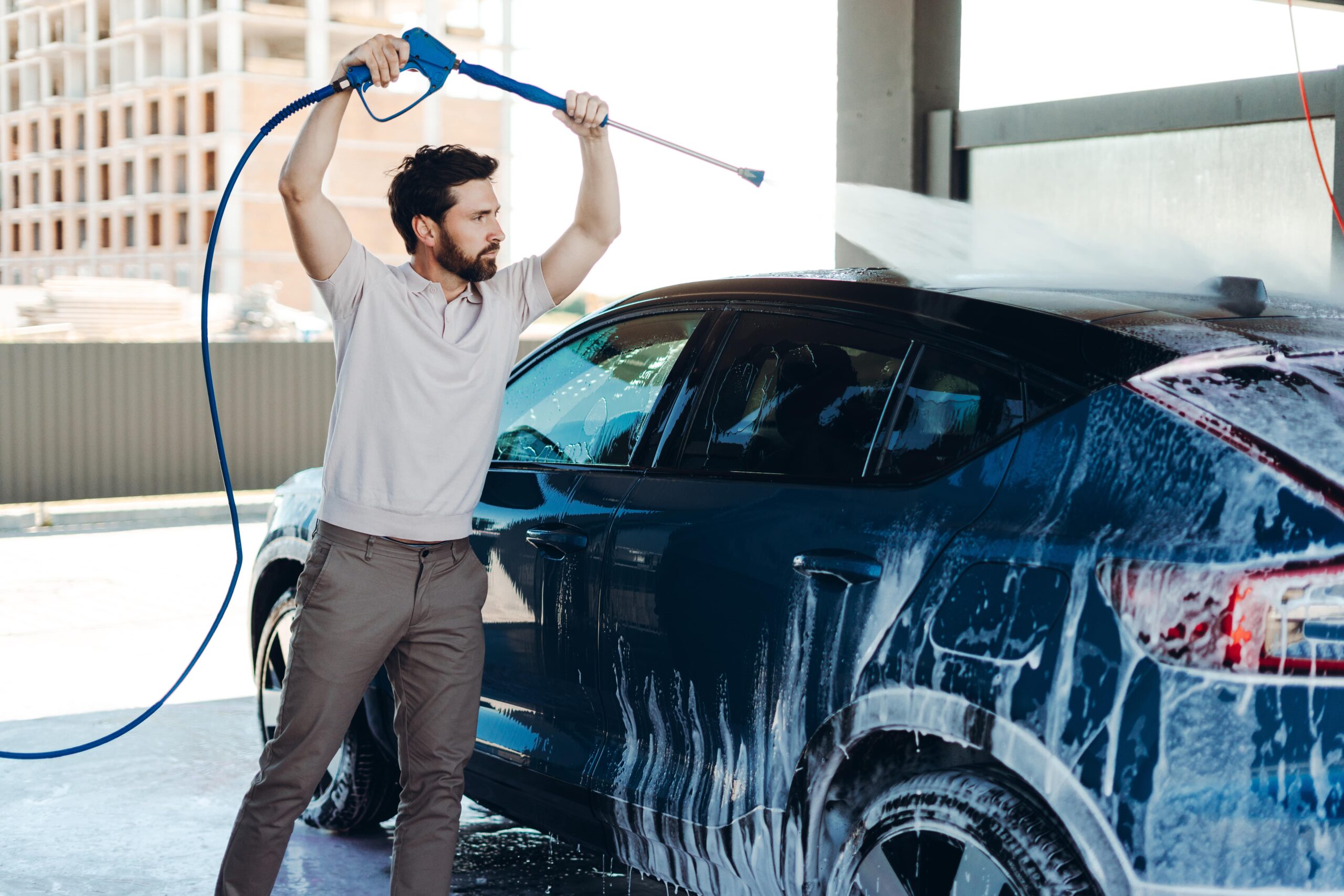 Man washing a car with a pressure washer in a self-serve bay